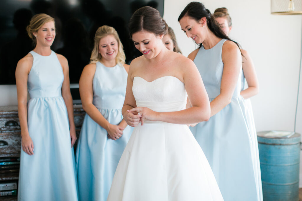 Bridesmaids help a bride with the back of her dress while she gets ready for her Bald Head Island Wedding.