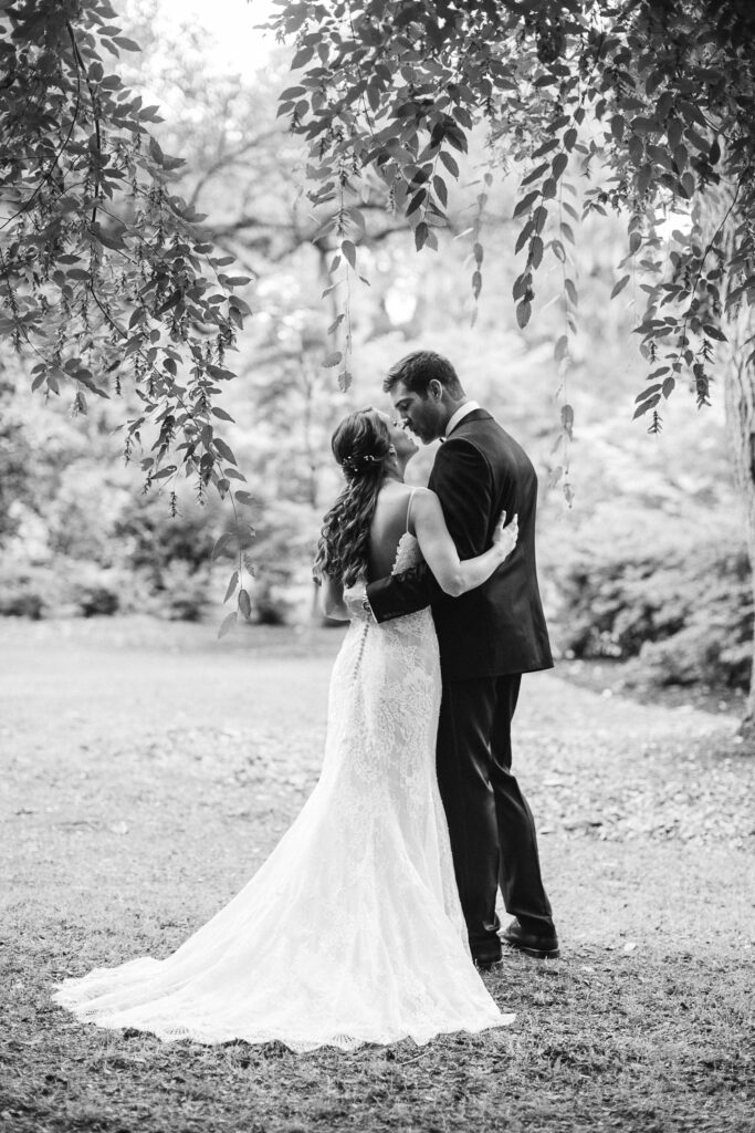 Bride and groom kiss under a tree in Airlie Gardens.