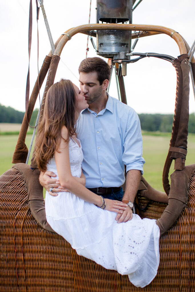 Engaged couple sits in a hot air balloon during their engagement session and shares a kiss.