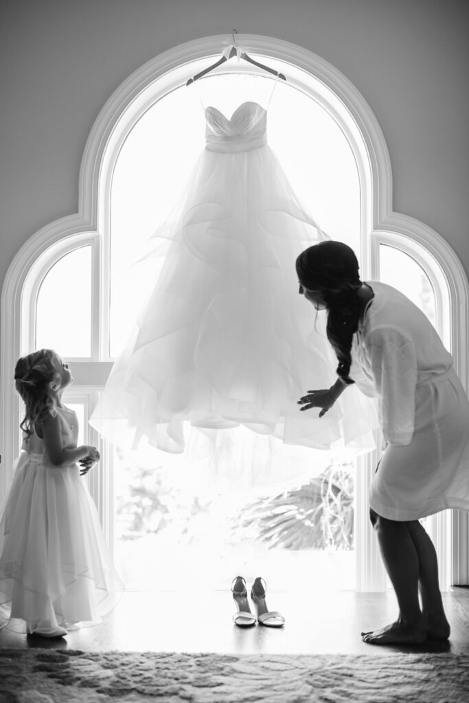 A flower girl looks up at the brides hanging dress in a beautiful wedding before the Wilmington NC wedding.