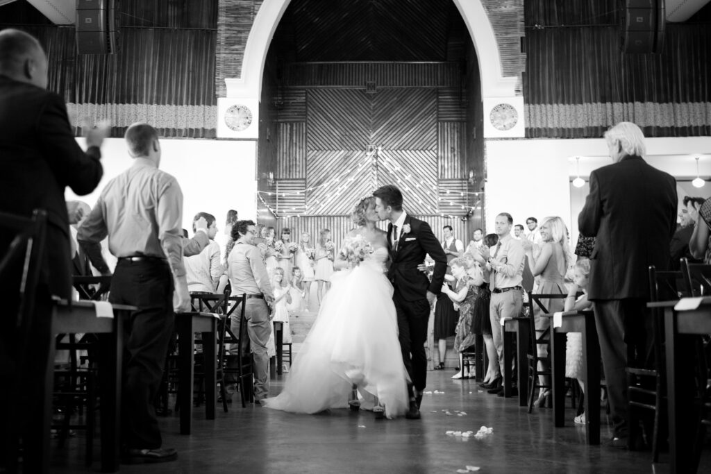 Bride and groom stop to kiss as they walk down the aisle in the Brooklyn Arts Center located in Wilmington NC.