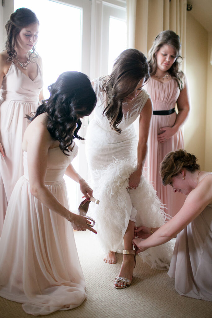 Bridesmaids help bride step into her wedding shoes before her wedding at the Atrium in Downtown Wilmington NC.