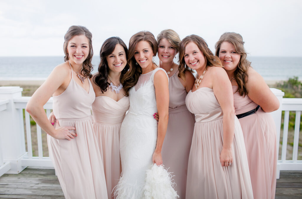 A bride and her bridesmaids stand on a balcony overlooking wrightsville beach nc after getting ready for her wedding