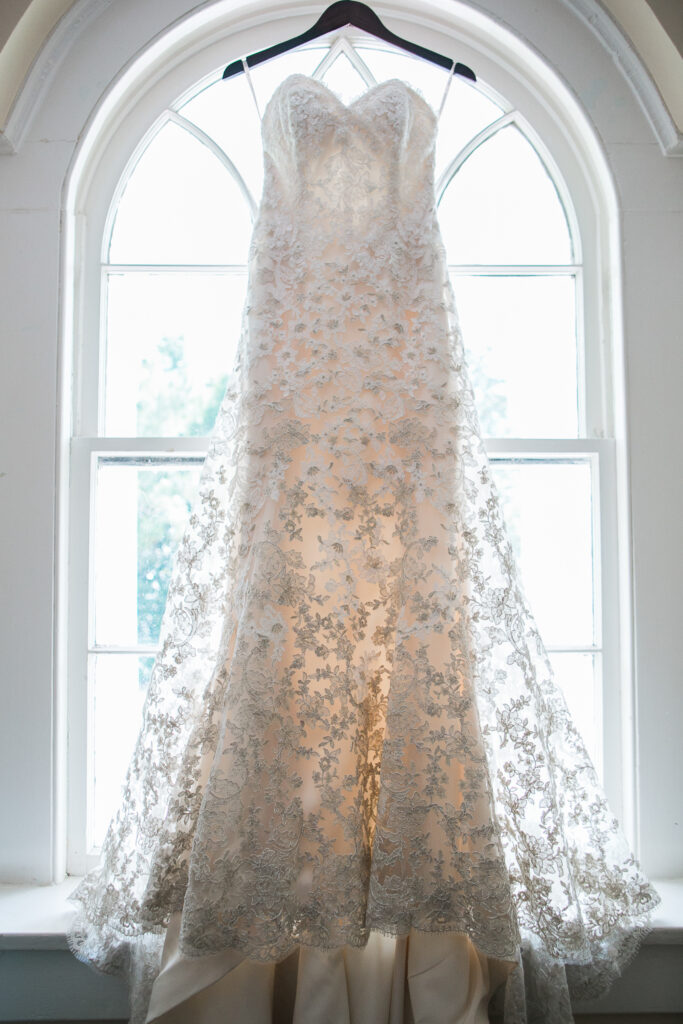 A wedding dress hangs in an arched window. While the bride gets ready for her Wilmington NC wedding all the details are photographed.