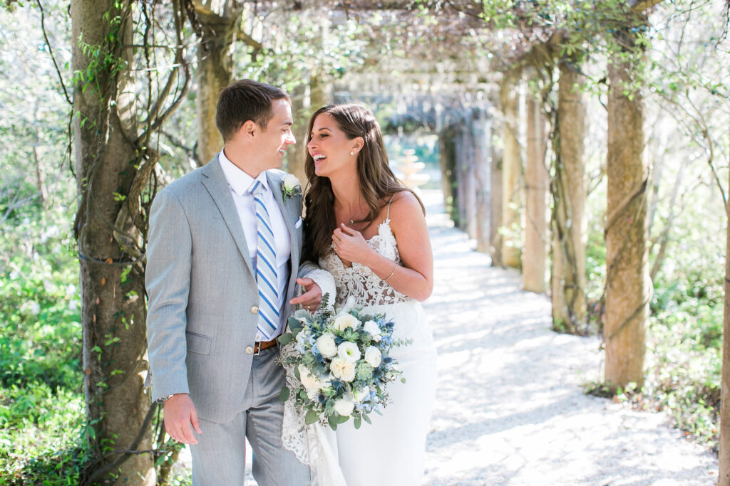 A bride laughs while standing with her groom in the Airlie Gardens pergola during their wedding.