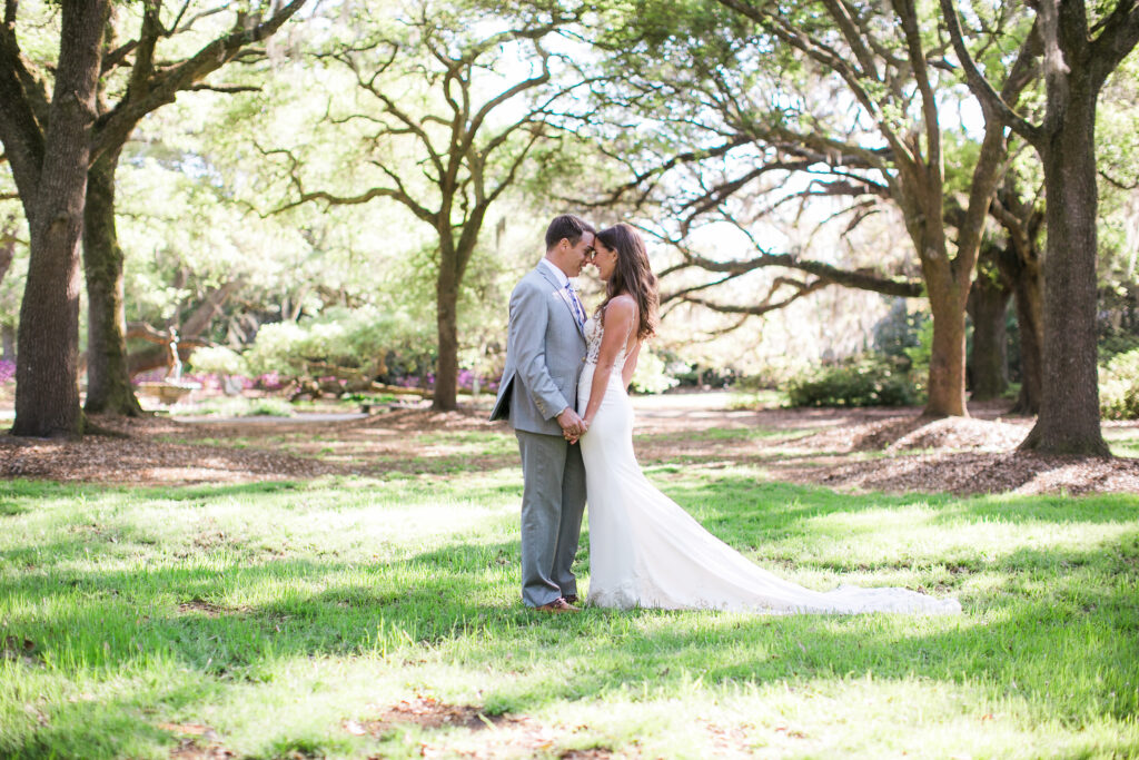 A bride and groom ebrace beneath a canopy of oak trees and spanish moss during their Airlie Gardens wedding day.