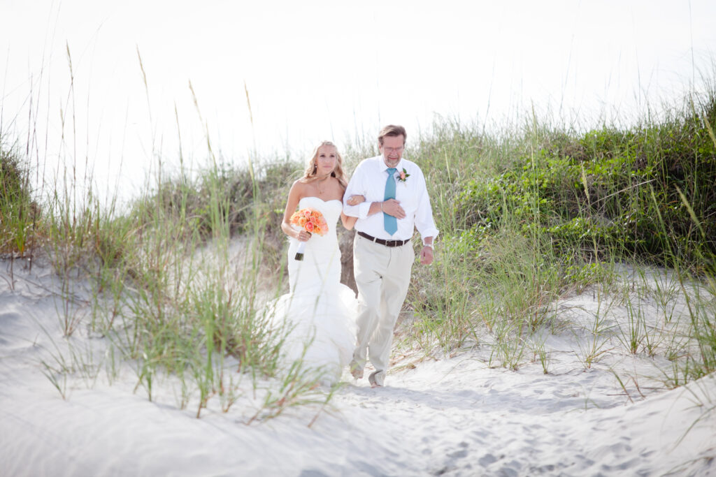 A father walks a bride through the dunes to her Shell Island Resort beach wedding