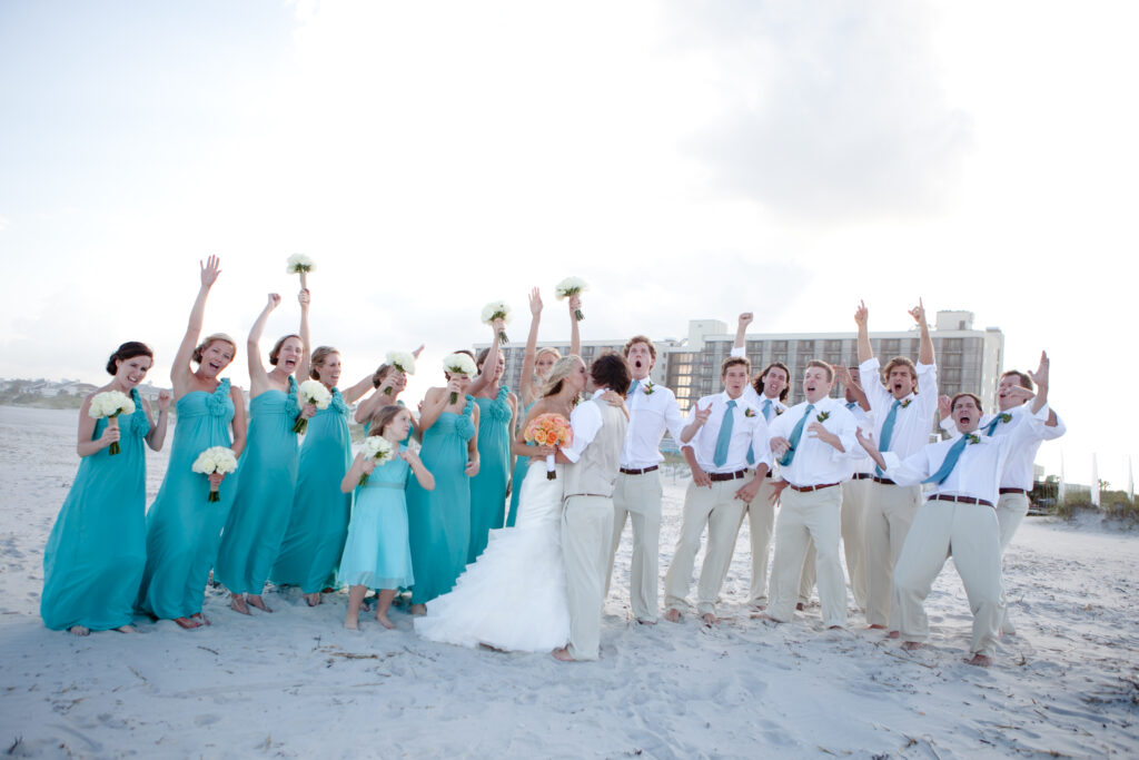 Bride and groom kiss while their wedding party cheers for them on Wrightsville Beach.